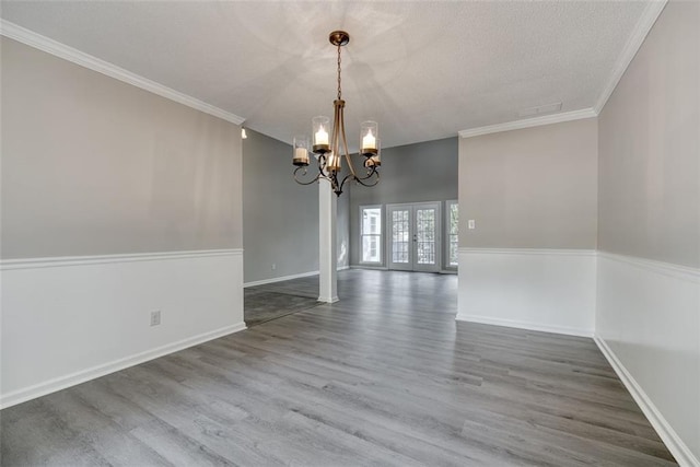 unfurnished dining area with ornamental molding, a chandelier, french doors, and hardwood / wood-style flooring