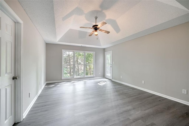 empty room featuring a textured ceiling, dark hardwood / wood-style floors, ceiling fan, and a tray ceiling