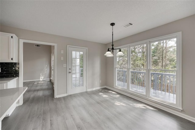 unfurnished dining area featuring hardwood / wood-style floors, a textured ceiling, plenty of natural light, and a notable chandelier