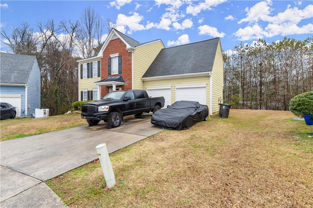 view of side of home featuring driveway, a garage, roof with shingles, a yard, and brick siding