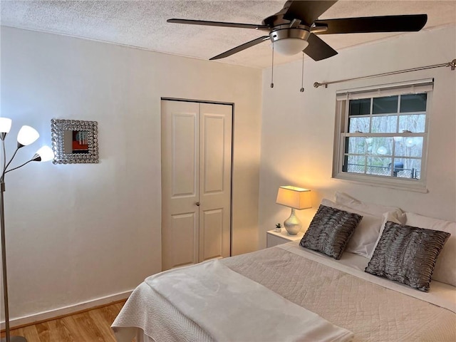 bedroom with wood finished floors, a closet, ceiling fan, a textured ceiling, and baseboards