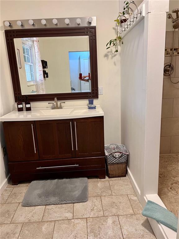 bathroom with vanity, baseboards, stone tile flooring, and tiled shower