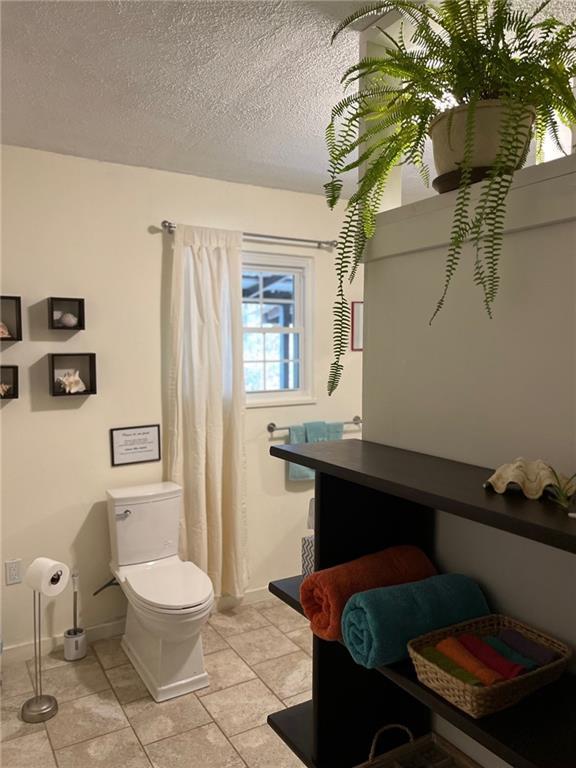 bathroom with toilet, baseboards, tile patterned floors, a textured ceiling, and a shower with shower curtain