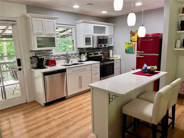 kitchen featuring appliances with stainless steel finishes, a sink, light countertops, light wood-style floors, and backsplash
