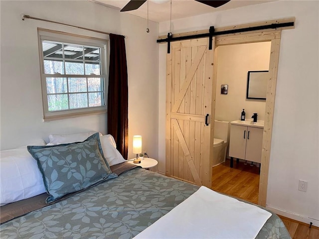 bedroom featuring a barn door, wood finished floors, baseboards, and ceiling fan