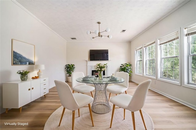 dining space with baseboards, light wood finished floors, an inviting chandelier, a fireplace, and ornamental molding