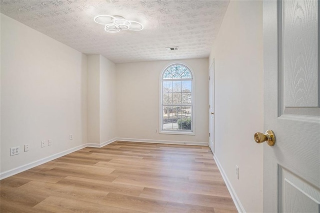 spare room featuring baseboards, light wood-style floors, visible vents, and a textured ceiling