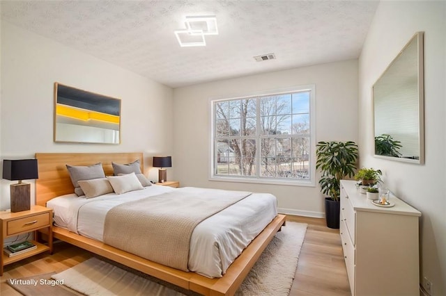 bedroom featuring light wood finished floors, visible vents, a textured ceiling, and baseboards