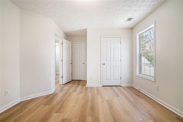 unfurnished bedroom with baseboards, visible vents, light wood finished floors, and a textured ceiling