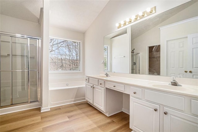 bathroom with a shower stall, lofted ceiling, wood finished floors, a bath, and a sink