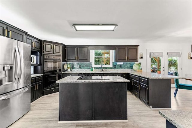 kitchen with black appliances, backsplash, a center island, a peninsula, and light wood finished floors