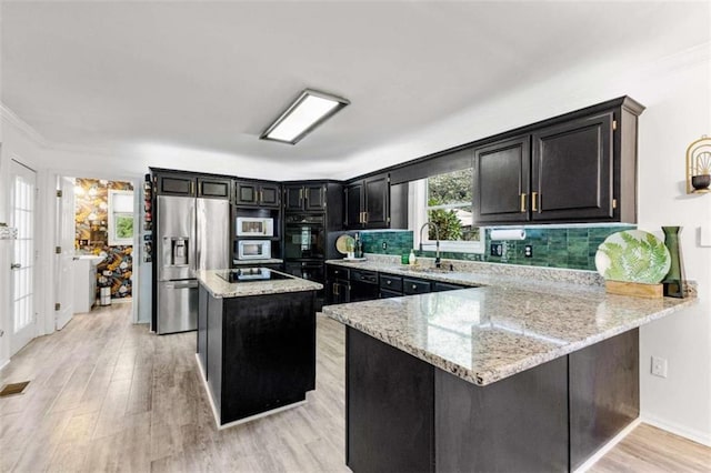 kitchen featuring backsplash, light stone countertops, appliances with stainless steel finishes, dark cabinetry, and a sink