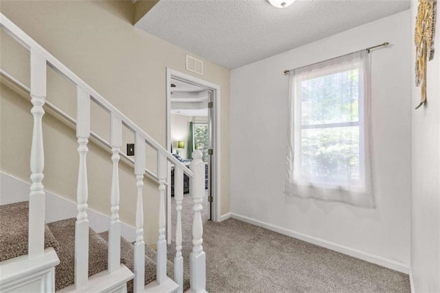 stairway with plenty of natural light, a textured ceiling, carpet, and visible vents