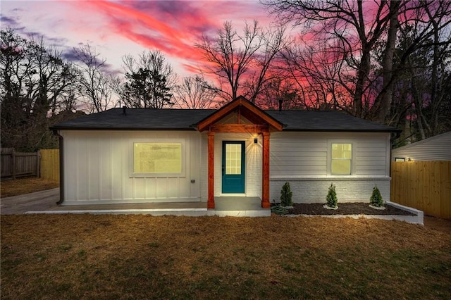 view of front of house with brick siding, fence, and a lawn