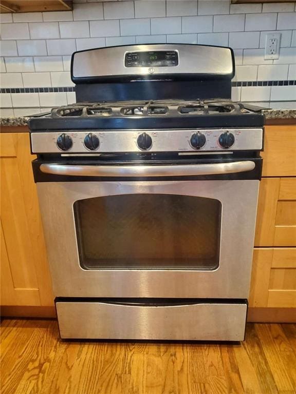 interior details featuring dark countertops, light wood-style flooring, tasteful backsplash, and stainless steel gas stove