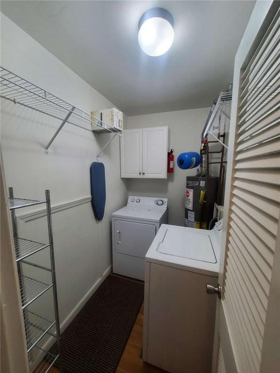 laundry area featuring baseboards, washing machine and clothes dryer, cabinet space, water heater, and dark wood-type flooring