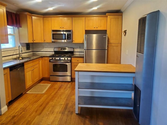 kitchen with wood finished floors, a sink, stainless steel appliances, backsplash, and butcher block counters