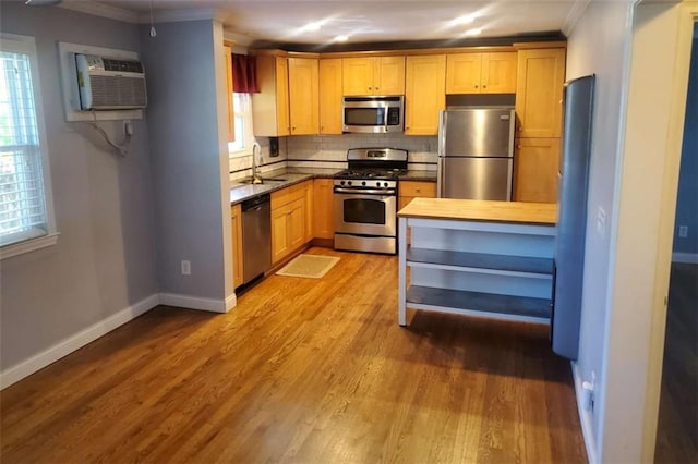 kitchen featuring ornamental molding, a sink, tasteful backsplash, wood finished floors, and appliances with stainless steel finishes