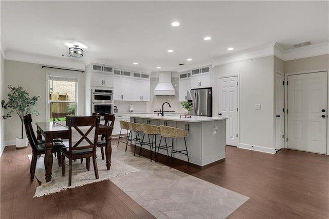 1105 Sterling Brooke Dr, Alpharetta, GA 30022 - kitchen with stainless steel appliances, custom exhaust hood, ornamental molding, light countertops, and an island with sink