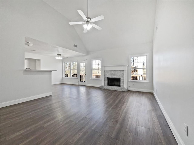 unfurnished living room featuring plenty of natural light, high vaulted ceiling, a stone fireplace, and dark hardwood / wood-style flooring