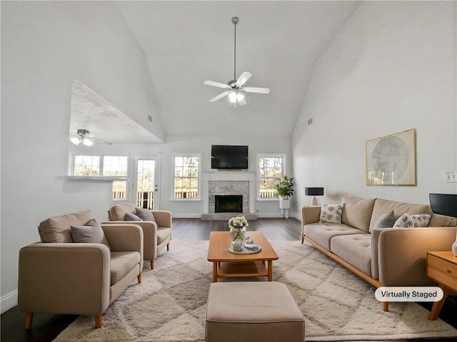 living room featuring ceiling fan, high vaulted ceiling, a stone fireplace, and light hardwood / wood-style floors