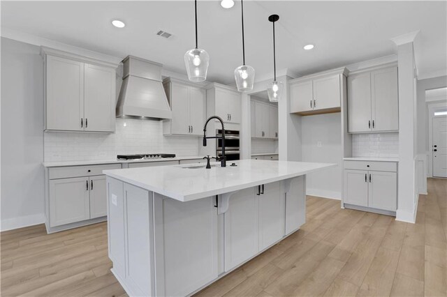 kitchen featuring a center island with sink, custom exhaust hood, light hardwood / wood-style floors, and tasteful backsplash