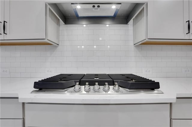 interior details with tasteful backsplash, light stone counters, white cabinets, and wall chimney range hood