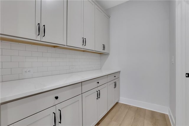 interior space with tasteful backsplash, light stone counters, white cabinets, and light hardwood / wood-style floors