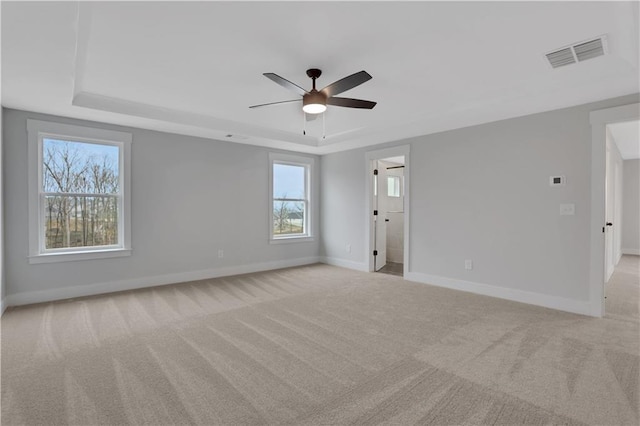 carpeted spare room featuring a tray ceiling, ceiling fan, and plenty of natural light