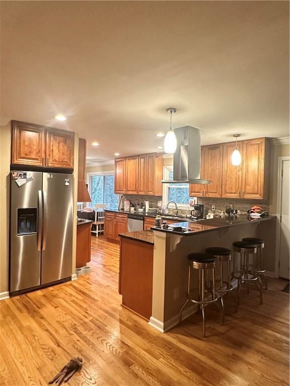 kitchen featuring appliances with stainless steel finishes, island range hood, decorative light fixtures, kitchen peninsula, and a breakfast bar