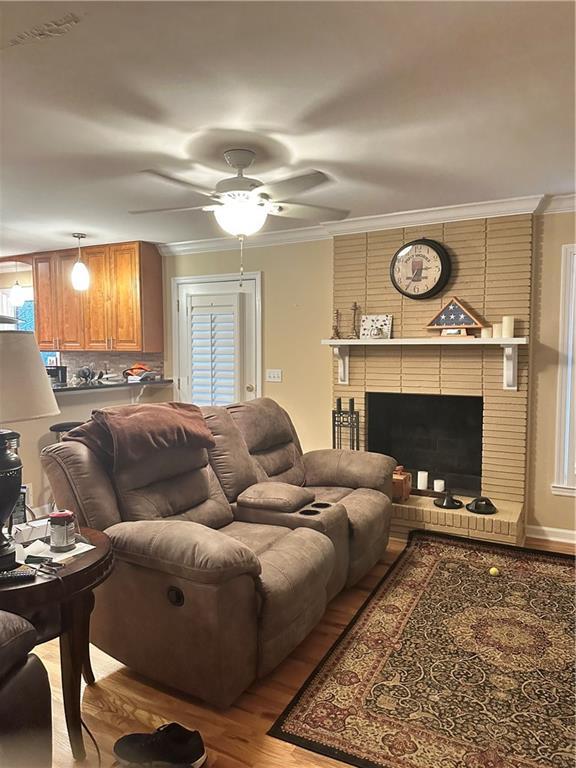 living room with light hardwood / wood-style floors, ornamental molding, ceiling fan, and a fireplace