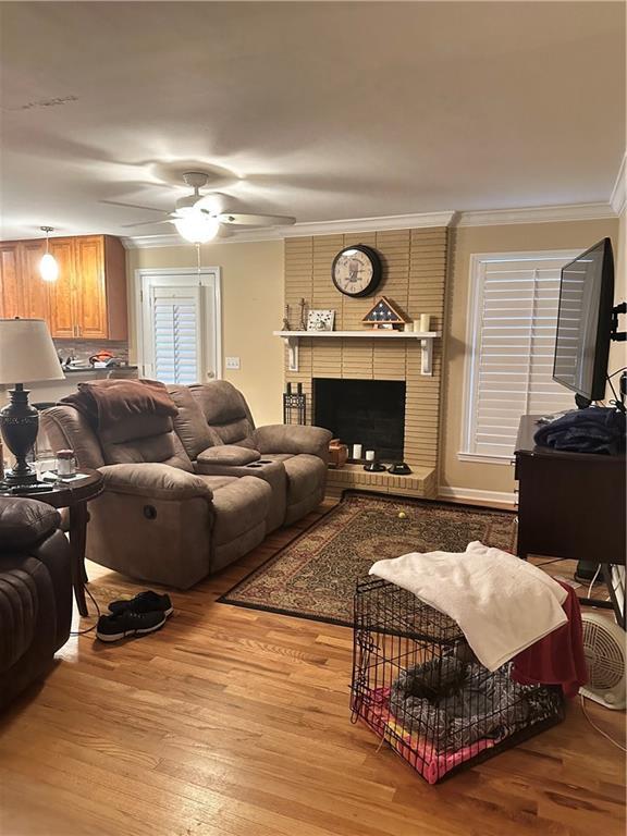 living room featuring light hardwood / wood-style floors, ornamental molding, ceiling fan, and a fireplace