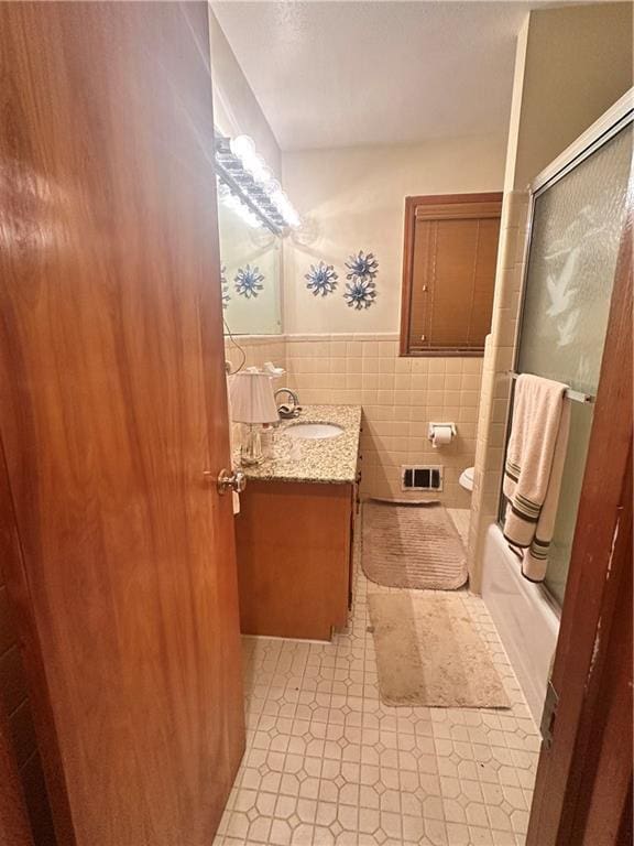 full bathroom with shower / bath combination with glass door, toilet, vanity, and tile walls