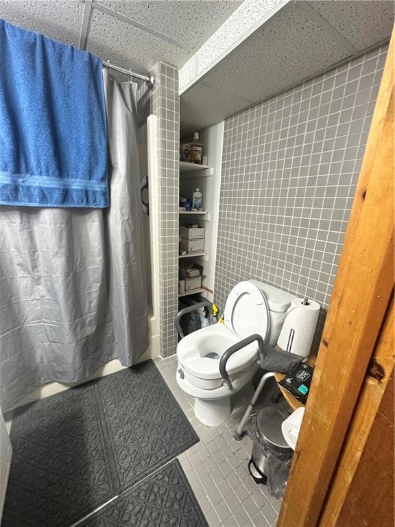 bathroom with tile patterned floors, toilet, a paneled ceiling, and shower / bathtub combination with curtain