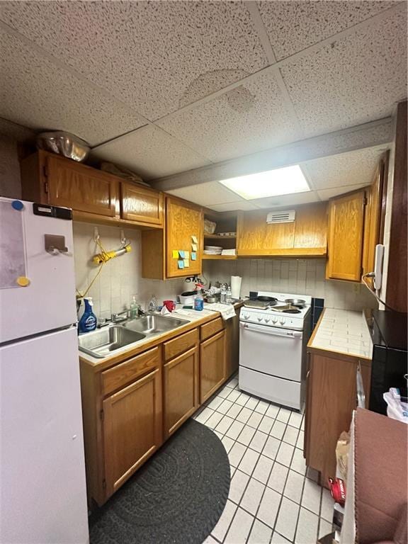 kitchen with sink, white appliances, a drop ceiling, and light tile patterned floors