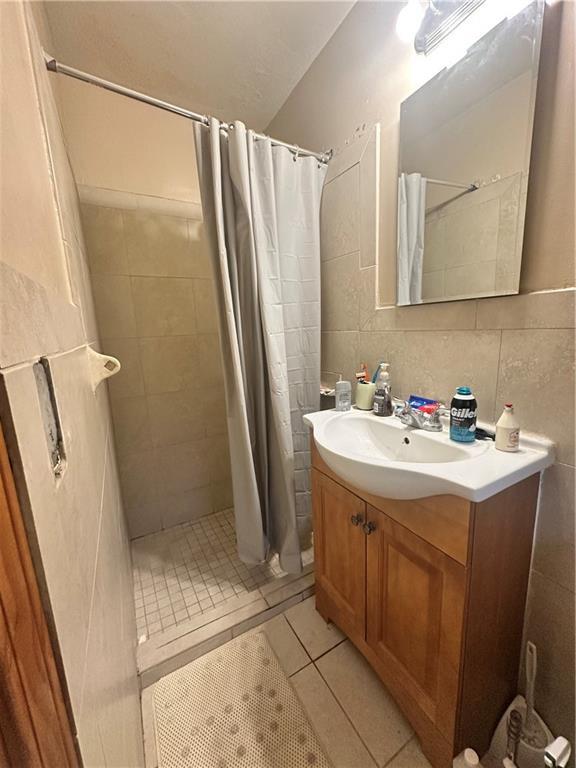 bathroom with tile patterned floors, vanity, decorative backsplash, tile walls, and walk in shower