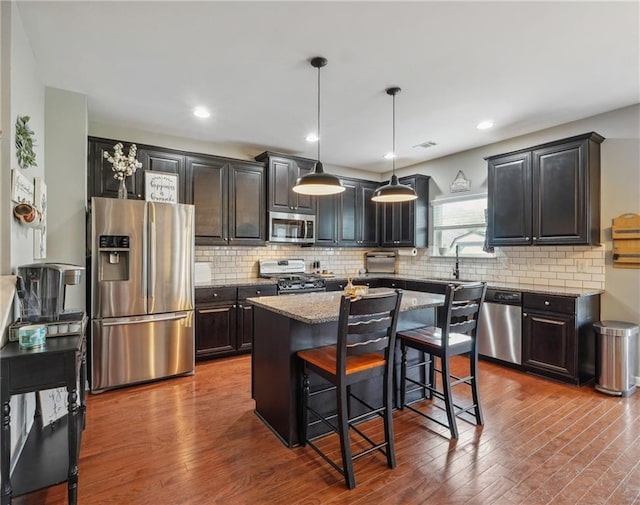 kitchen with pendant lighting, hardwood / wood-style floors, a center island, a breakfast bar area, and stainless steel appliances