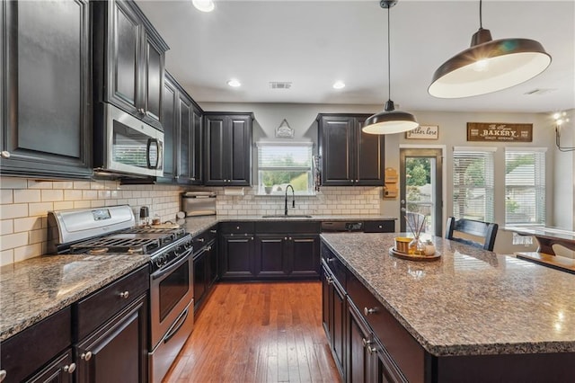 kitchen featuring appliances with stainless steel finishes, sink, stone countertops, decorative light fixtures, and a kitchen island