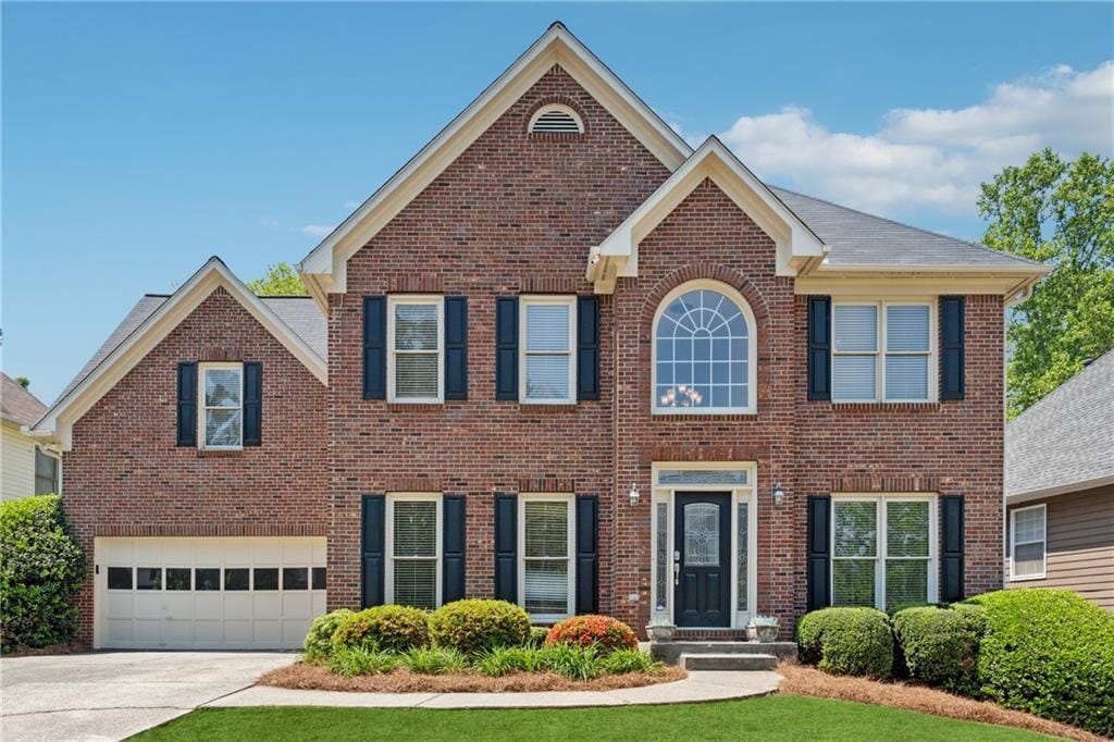 colonial home with an attached garage, brick siding, and driveway