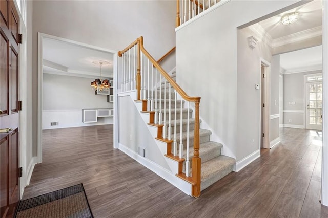 stairs with hardwood / wood-style floors, crown molding, and a chandelier