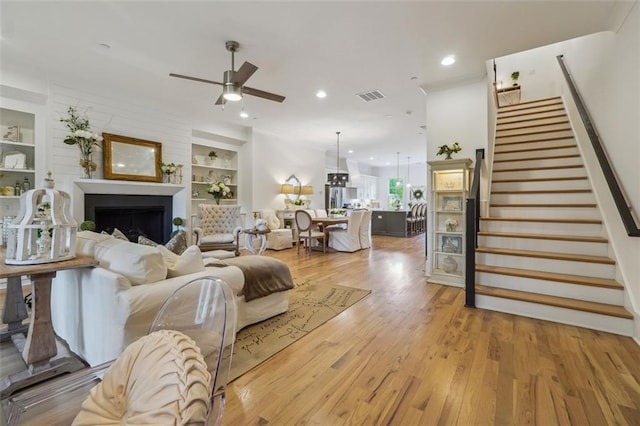 living room featuring built in features, light wood-type flooring, and ceiling fan with notable chandelier