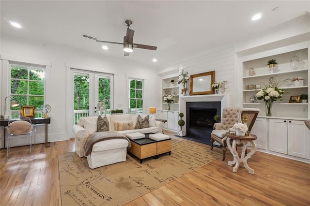 living room with built in shelves, ceiling fan, and light hardwood / wood-style floors