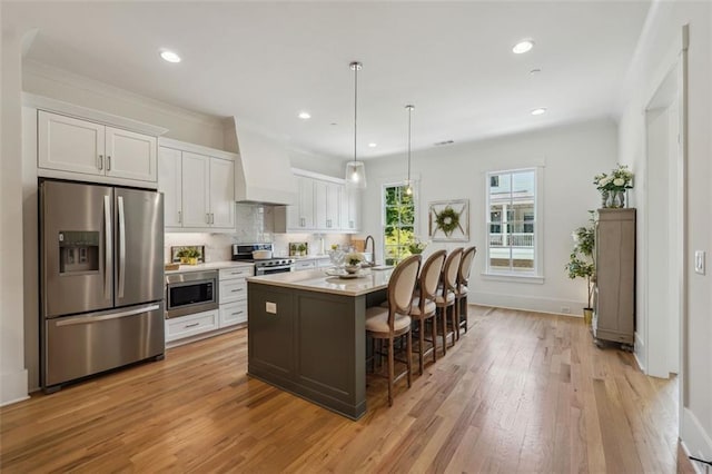 kitchen with a kitchen island with sink, stainless steel appliances, a kitchen breakfast bar, white cabinets, and light hardwood / wood-style flooring