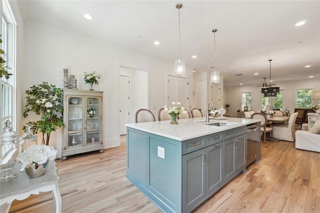 kitchen with hanging light fixtures, sink, an island with sink, and light hardwood / wood-style flooring