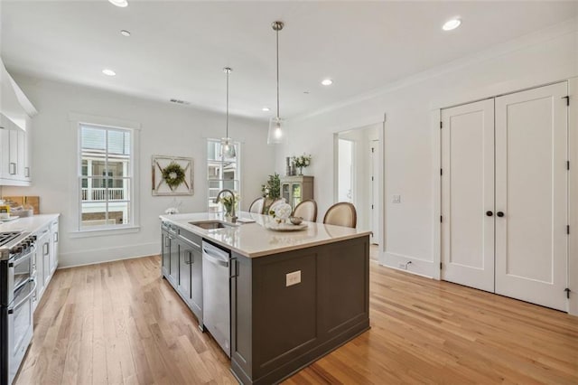 kitchen with light hardwood / wood-style floors, sink, appliances with stainless steel finishes, decorative light fixtures, and a kitchen island with sink