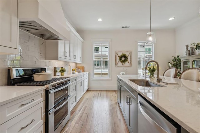 kitchen with white cabinetry, appliances with stainless steel finishes, custom range hood, light wood-type flooring, and pendant lighting