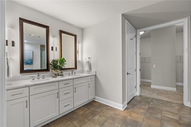 bathroom featuring a walk in closet, a sink, baseboards, and double vanity