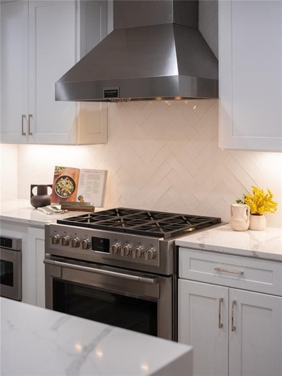 kitchen with wall chimney exhaust hood, appliances with stainless steel finishes, white cabinets, and decorative backsplash