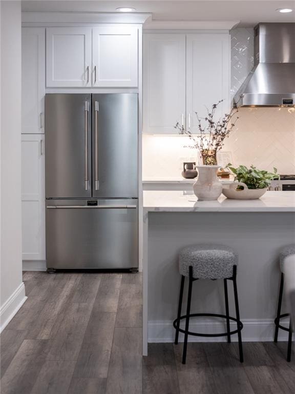 kitchen featuring dark wood finished floors, wall chimney exhaust hood, high end refrigerator, white cabinetry, and a kitchen bar
