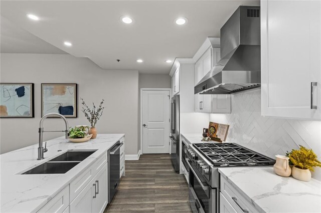 kitchen with a sink, high quality appliances, white cabinets, wall chimney range hood, and light stone countertops